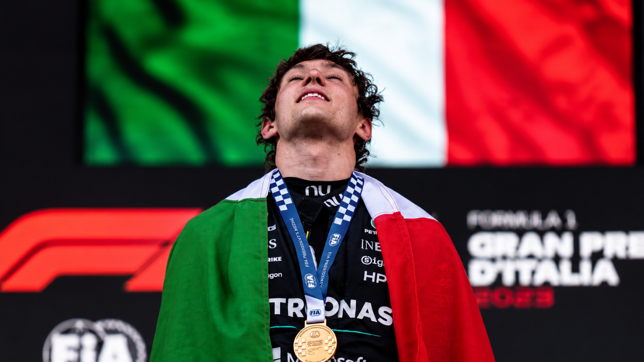 Kimi Antonelli sul podio con la bandiera tricolore sulle spalle e una medaglia d’oro al collo. 
