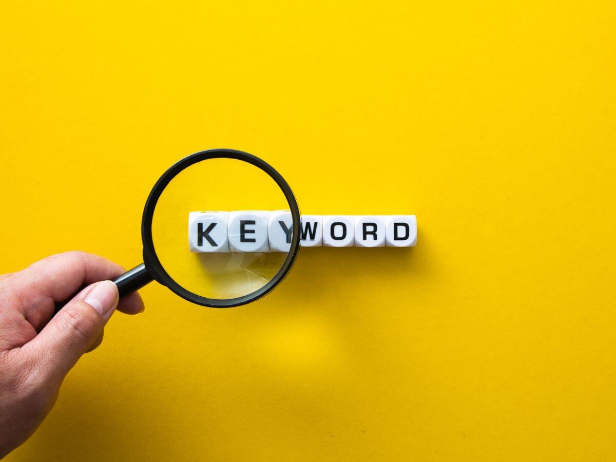 Photo of a magnifying glass held over letter tiles spelled keyword