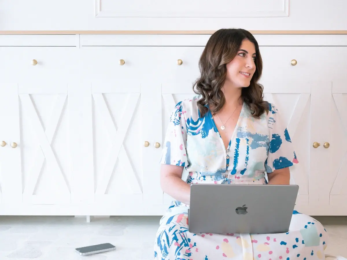 Photo of Hayley Philip working on her laptop while sitting on the floor and smiling, looking on her right