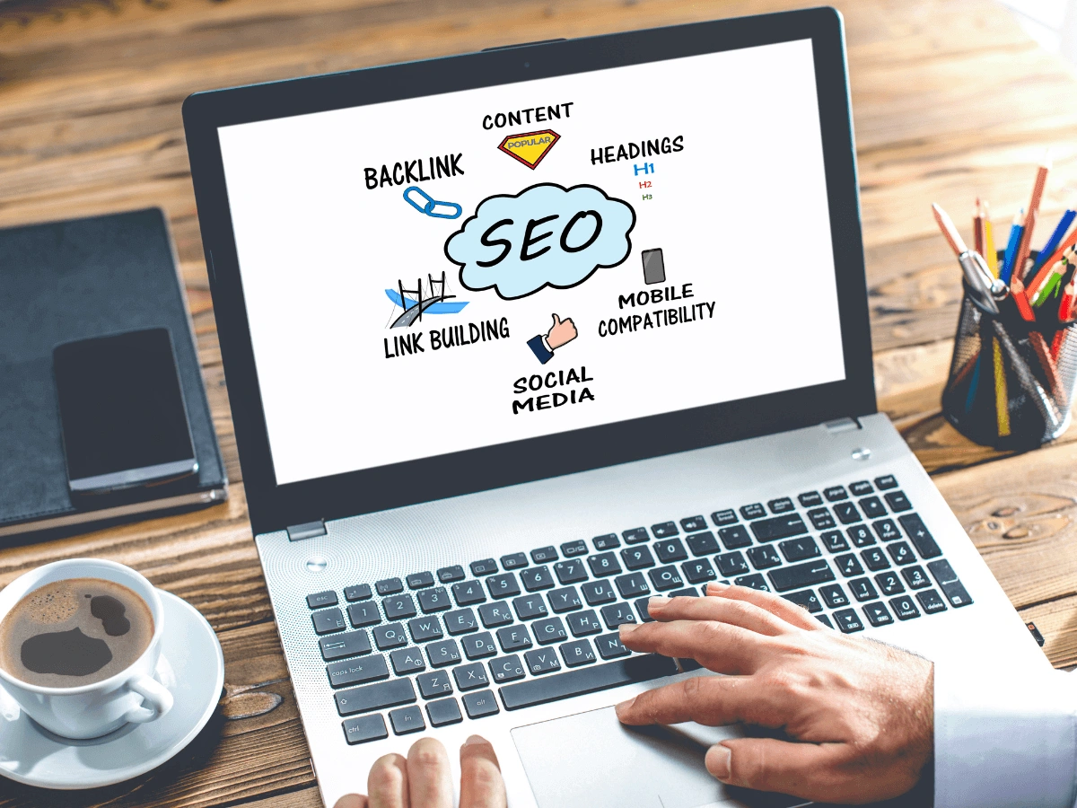 Laptop screen displaying an SEO diagram with key elements like content, backlinks, headings, link building, mobile compatibility, and social media, with a person's hands typing on the keyboard.