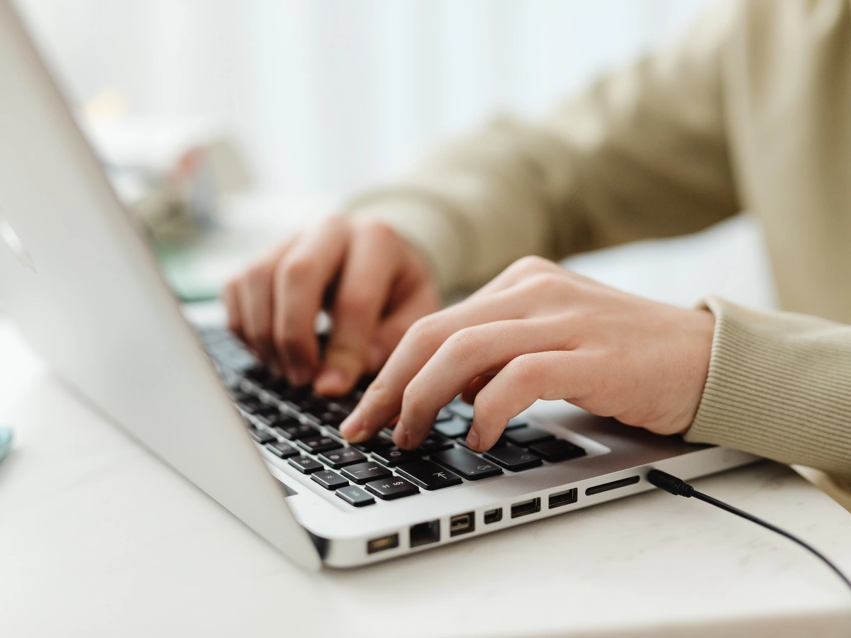 Close-up of hands typing on a laptop keyboard, focused on the fingers pressing the keys.