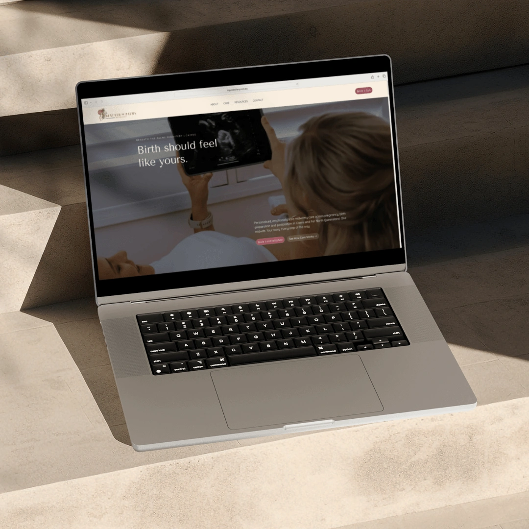Laptop mockup on sunlit stone steps displaying the Beneath the Palms Midwifery homepage hero section, reading "Birth should feel like yours"