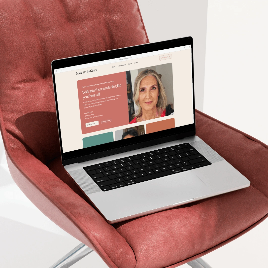 Laptop mockup on a terracotta chair displaying the Make Up by Kirsty homepage hero section, reading "Walk into the room feeling like your best self"