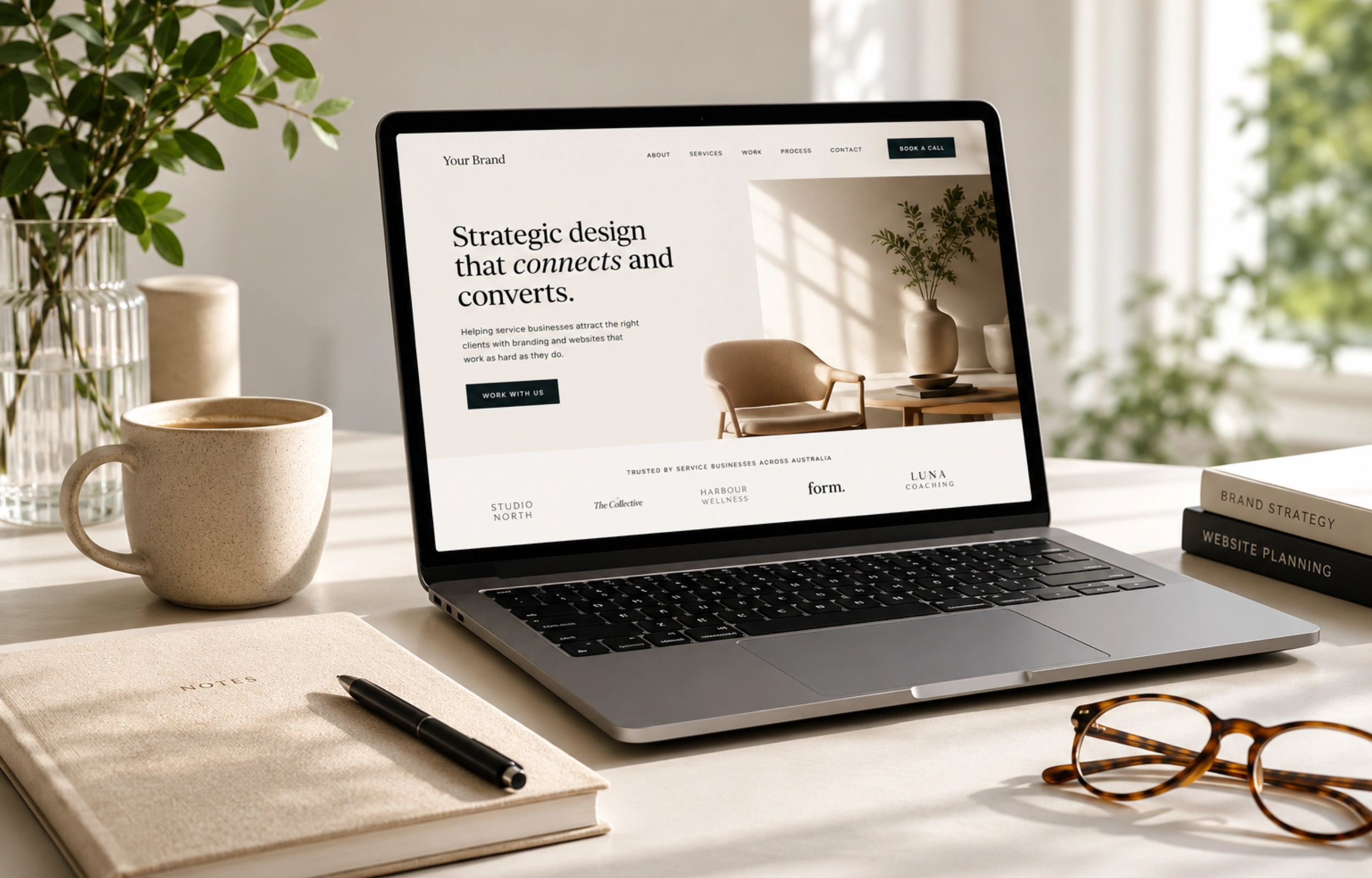 Laptop displaying an example homepage with the headline "Strategic design that connects and converts," featuring a client logo trust bar and a lifestyle image of a living room