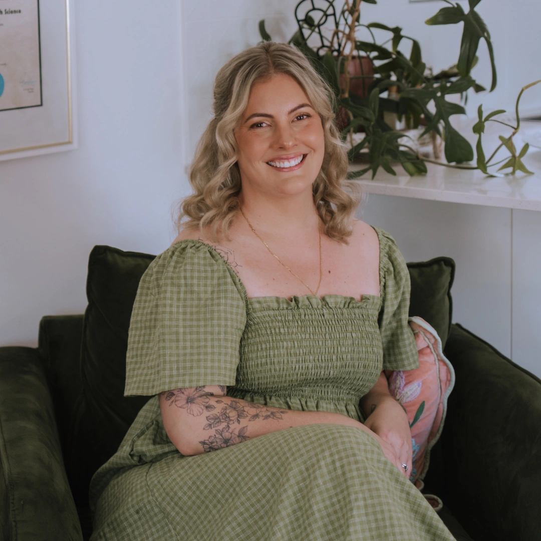 Portrait of Caitlin Mason, midwife at Beneath the Palms Midwifery, smiling and seated on a green velvet armchair
