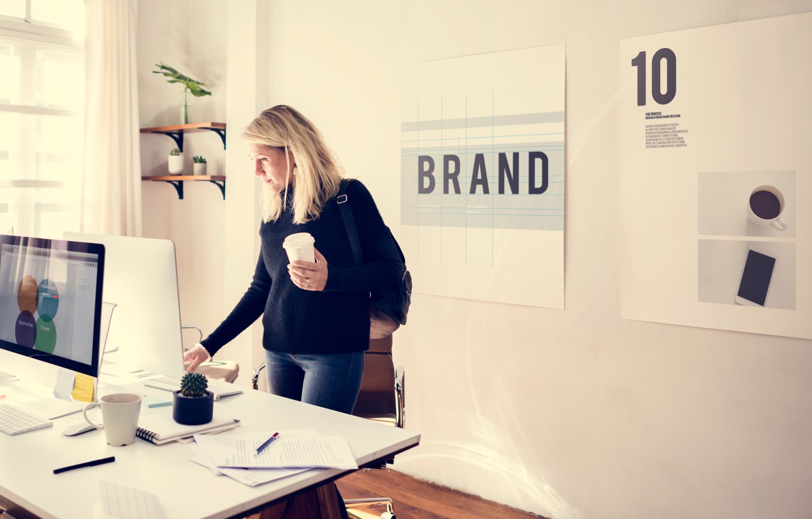 Logo vs brand identity: business owner at a desk in a bright studio with a BRAND poster on the wall