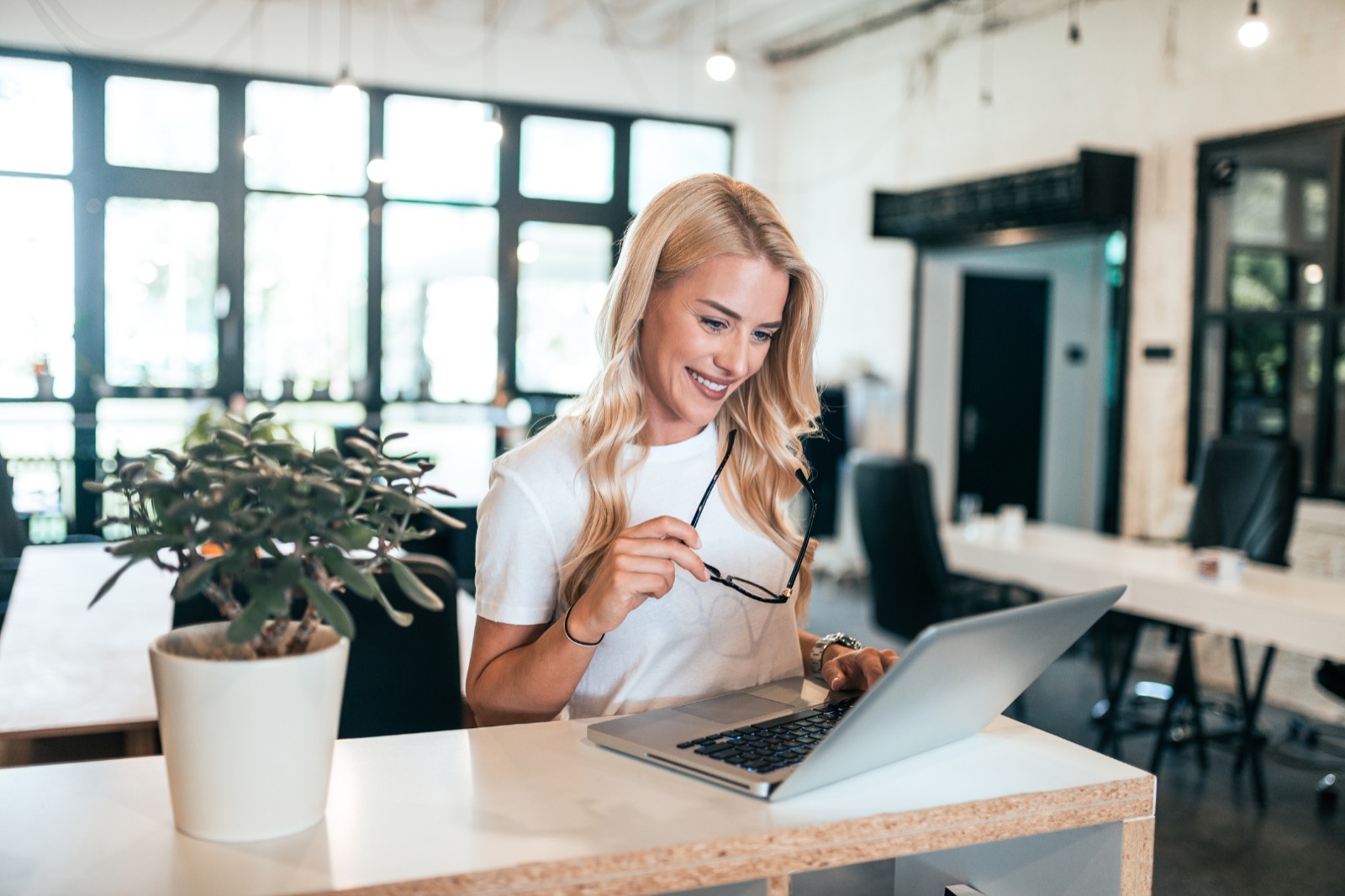 Domain email address: woman smiling at a laptop at a standing desk in a bright, open plan office
