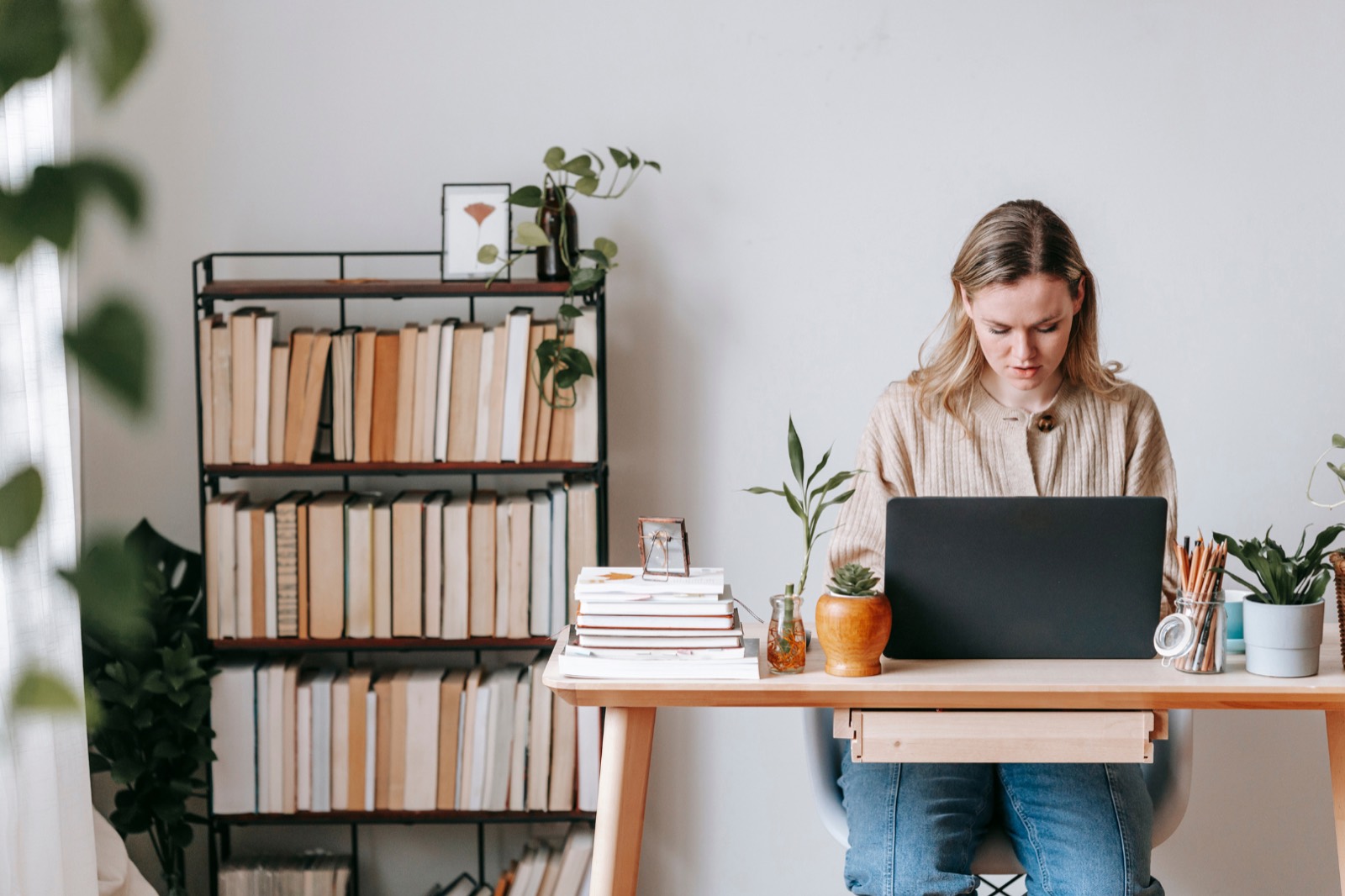 How to respond to a bad Google review: woman focused on a laptop at a tidy desk beside a bookshelf and indoor plants