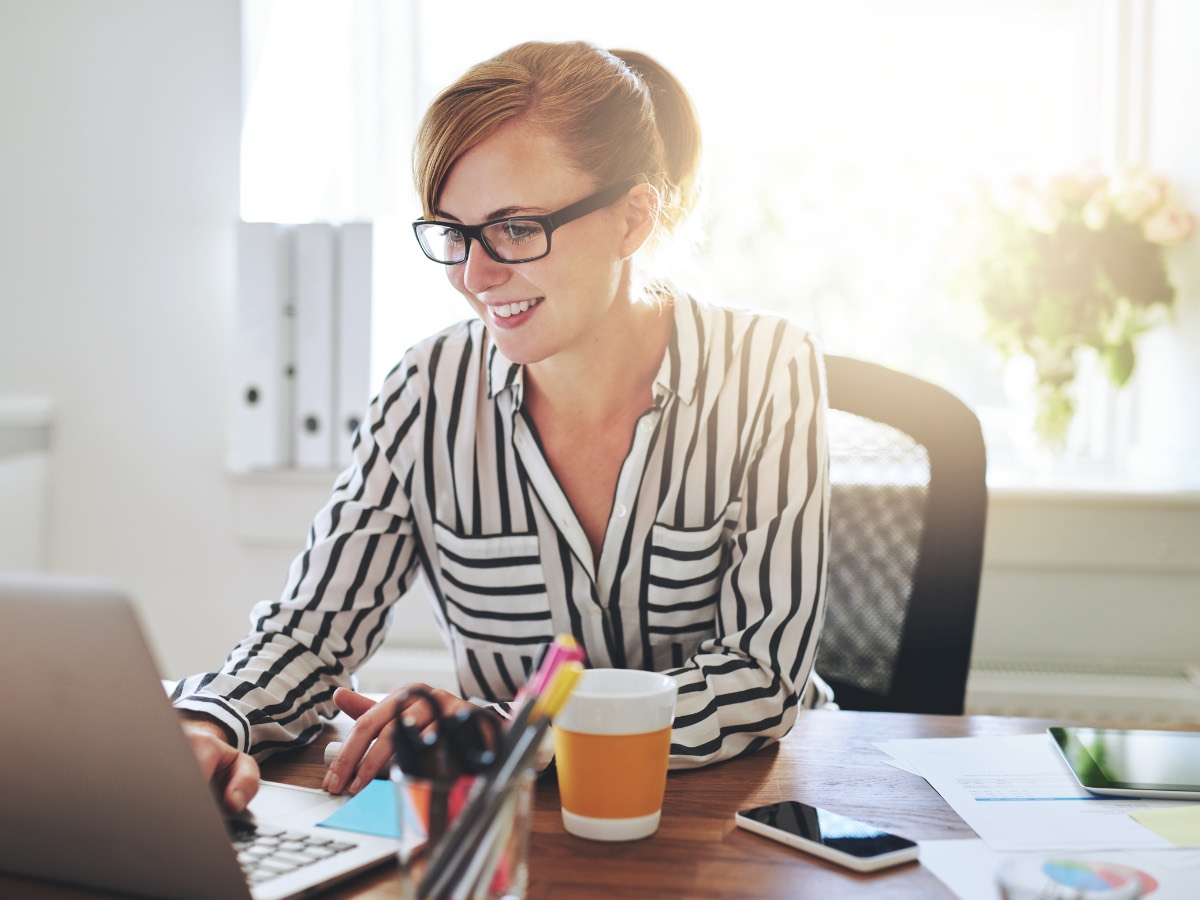 Smiling woman in glasses working on a laptop at an office desk