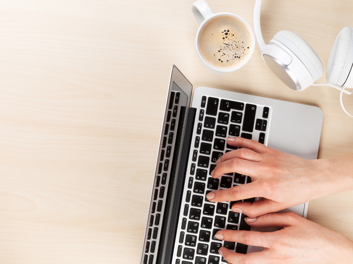 Overhead view of hands typing on a laptop with a coffee and headphones