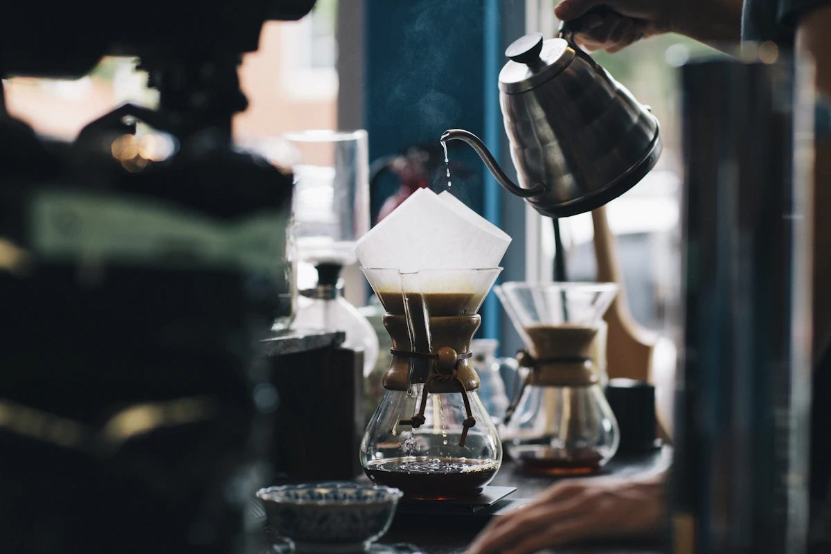 How to screen clients: a barista pouring hot water from a gooseneck kettle into a paper coffee filter on a glass pour-over brewer