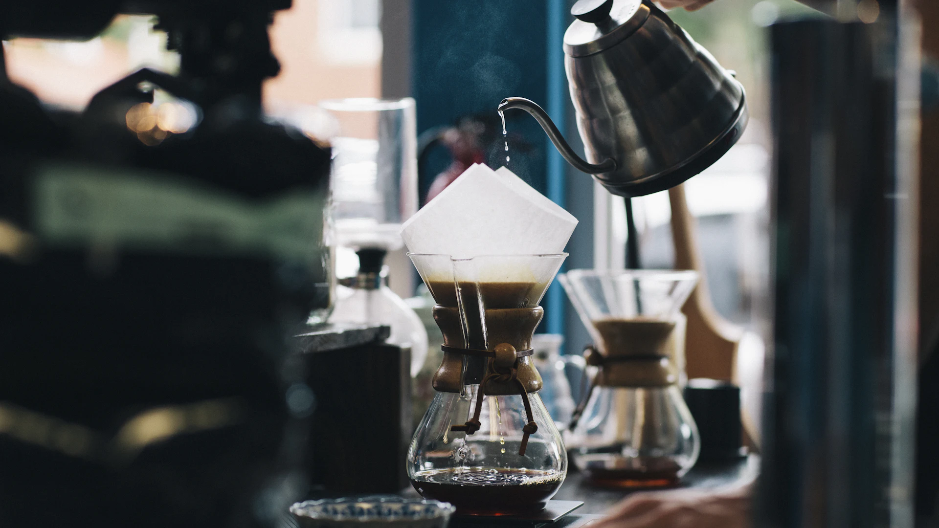How to screen clients: a barista pouring hot water from a gooseneck kettle into a paper coffee filter on a glass pour-over brewer