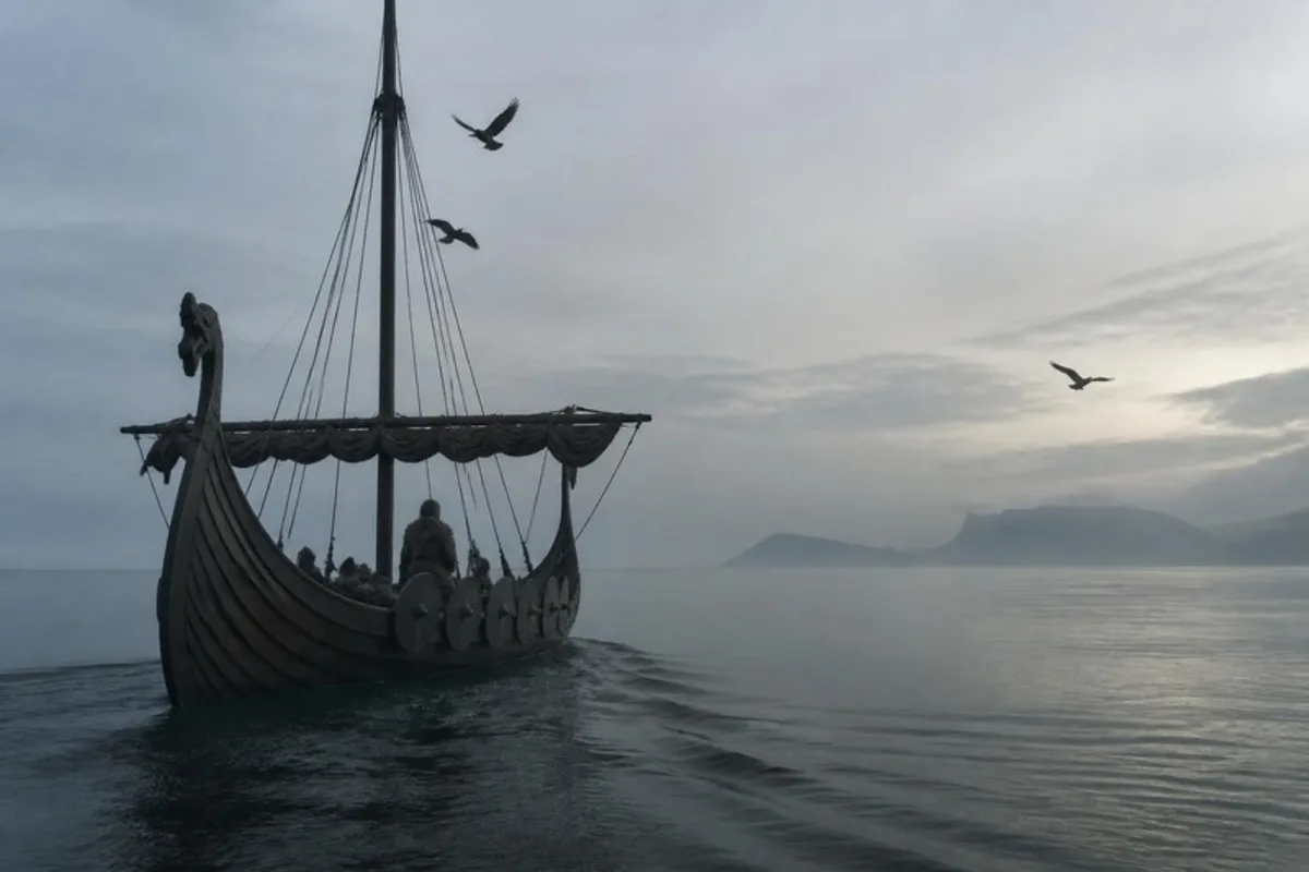 A Norse longship on a misty sea, with two ravens circling the mast and a third flying ahead towards the coast