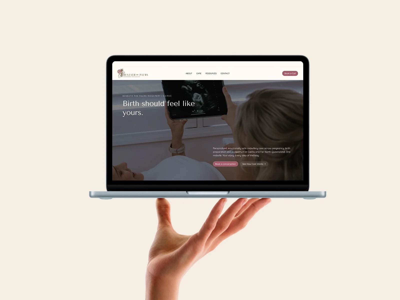 A hand holding a laptop showing the Beneath the Palms Midwifery homepage, 'Birth should feel like yours.'