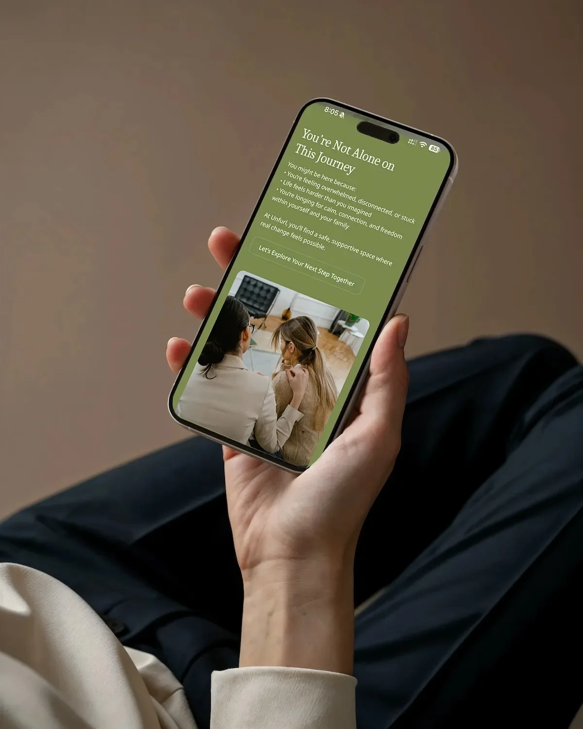 Hand holding a phone showing the Unfurl mobile site, 'You're Not Alone on This Journey'