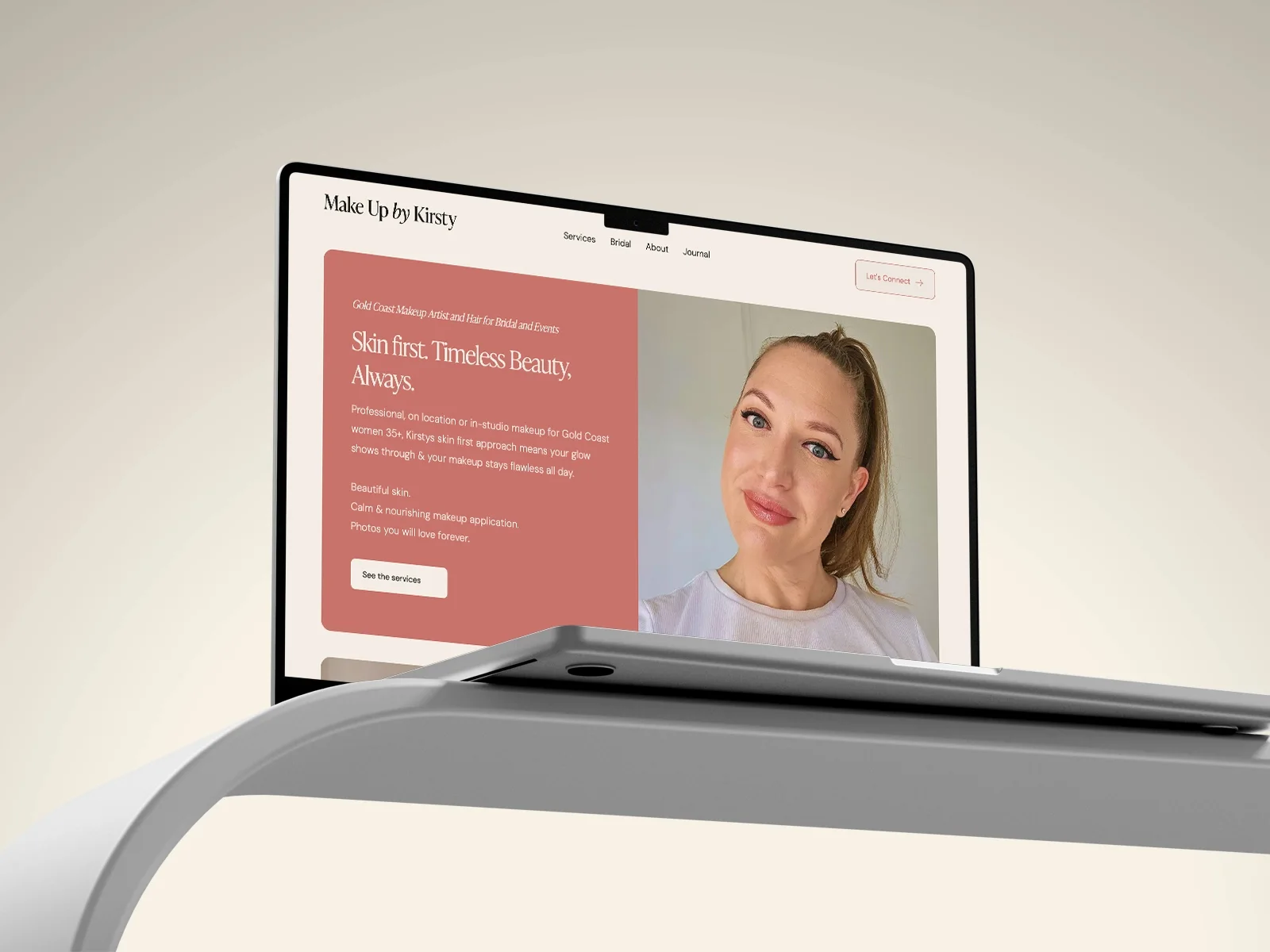 Laptop on a curved stand showing the Make Up by Kirsty homepage, 'Skin first. Timeless Beauty, Always.'
