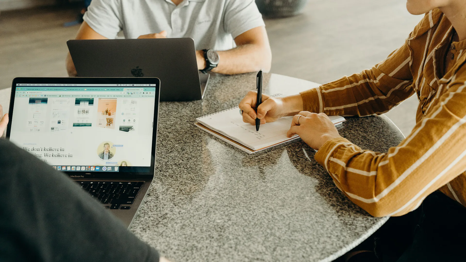 Three people at a round table planning a website, with a laptop open and notes being written