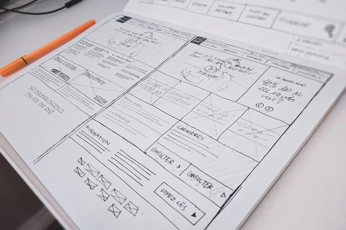 Hand-drawn website wireframe sketched on paper beside an orange pen