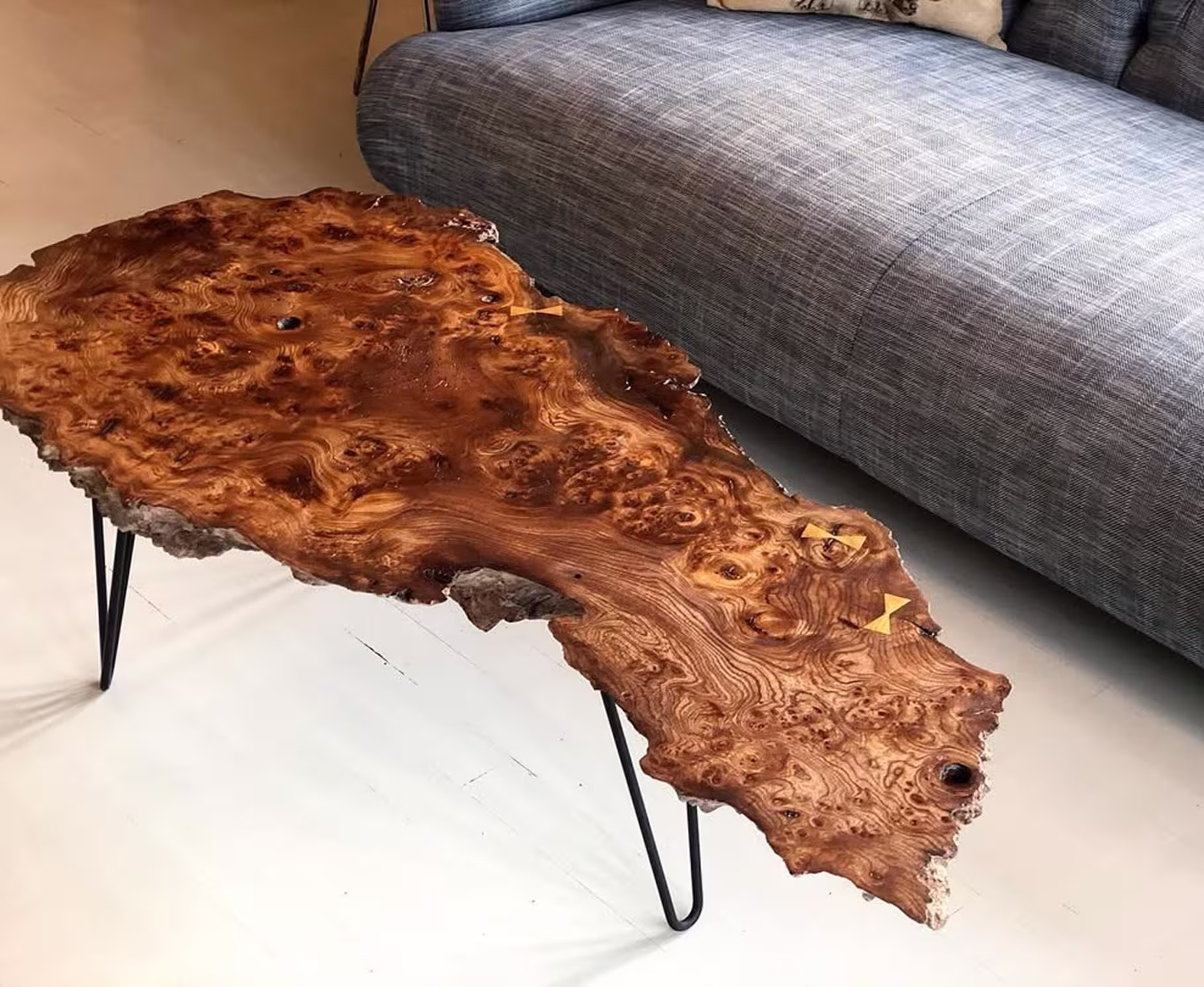 Live edge wooden coffee table with natural grain patterns and hairpin metal legs next to a gray couch.