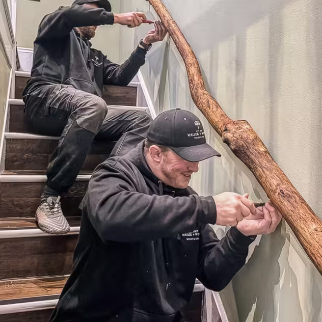 Alex and Tom installing a rustic wooden handrail on an indoor staircase.