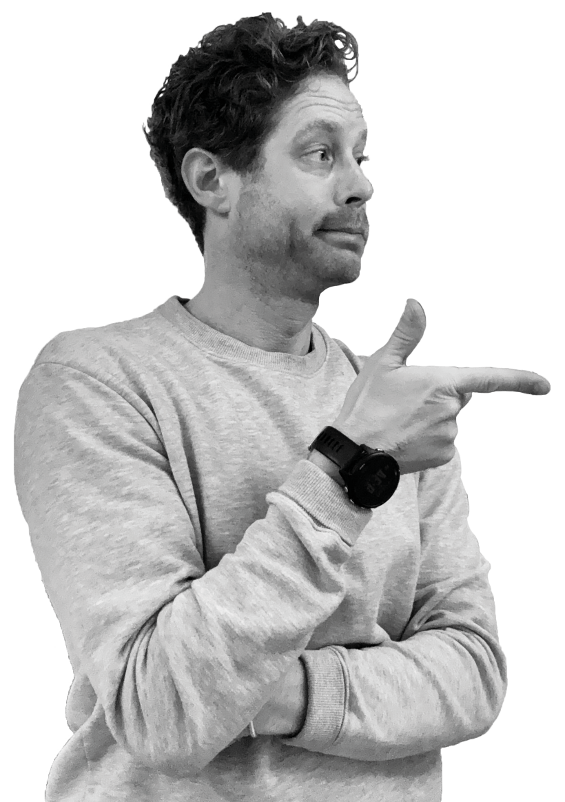 Man in gray sweatshirt with curly hair pointing to his right with a confident expression.