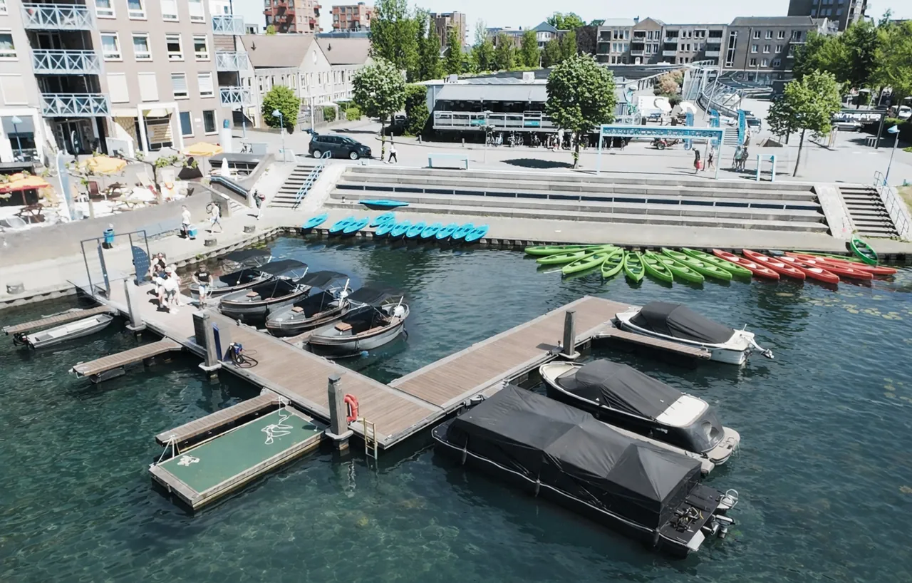 Haven aan de Vecht met aanlegsteiger, roeiboten, motorboten, sups en zitbanken aan de kade in Hardenberg met het Outdoor Kaffee op de achtergrond.