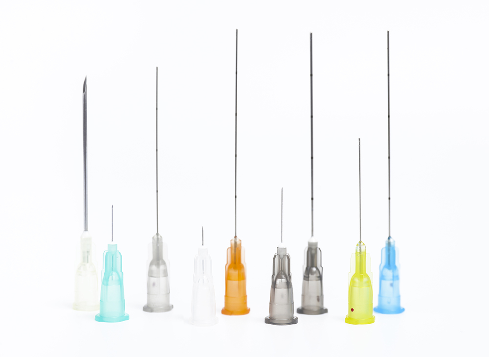 A row of nine different medical needles with various colored plastic bases and needle sizes on a white background.