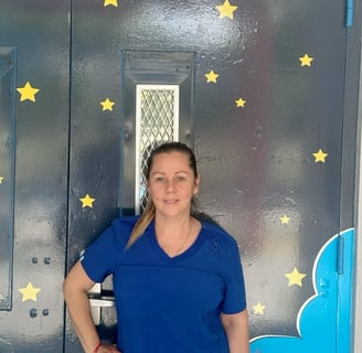 Woman in blue scrub top standing in front of a dark wall decorated with yellow stars and a blue cloud design.