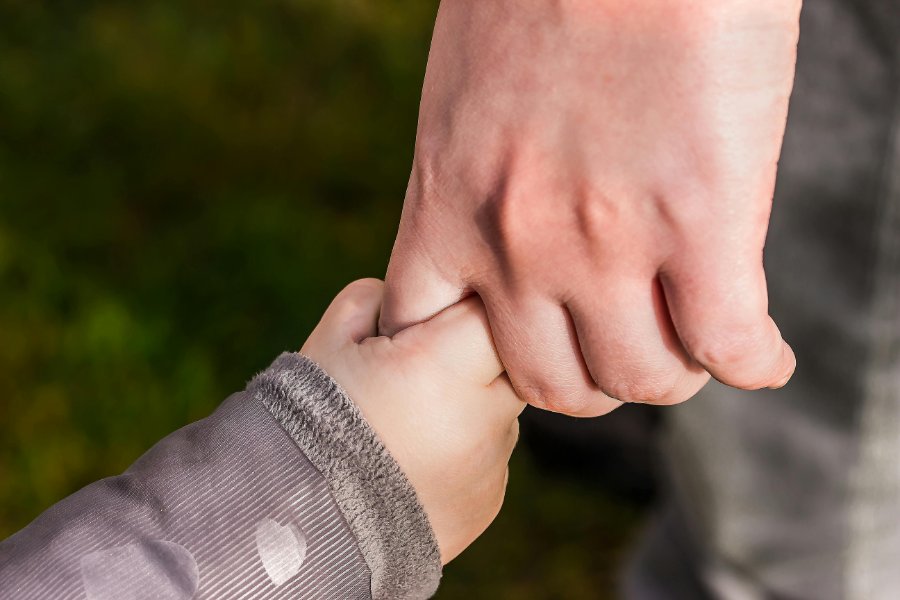 Child's hand holding an adult's hand outdoors with blurred green background.