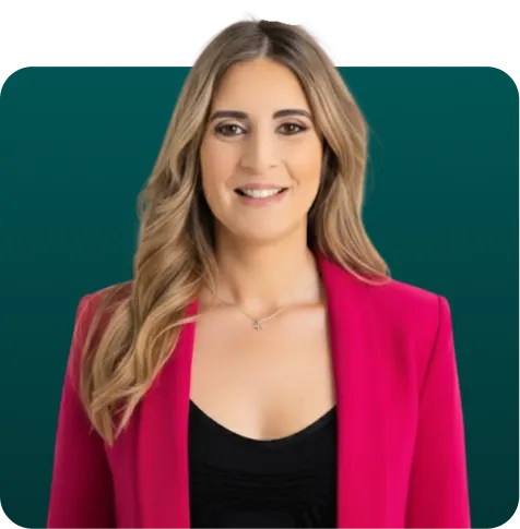 Smiling woman with long wavy hair wearing a bright pink blazer and black top against a teal background.