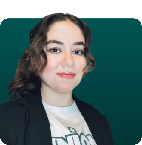 Smiling woman with curly dark brown hair wearing a black blazer and white printed shirt against a dark teal background.