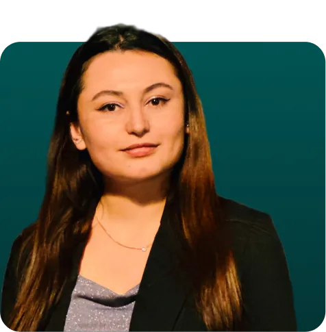Woman with long dark hair wearing a gray knit sweater and small necklace, smiling slightly against a teal background.