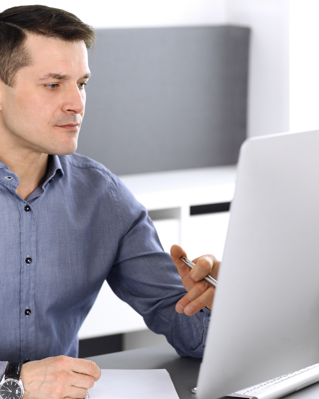 Stressed woman with blonde hair sitting at a table with documents and a laptop, holding her forehead in an office setting.