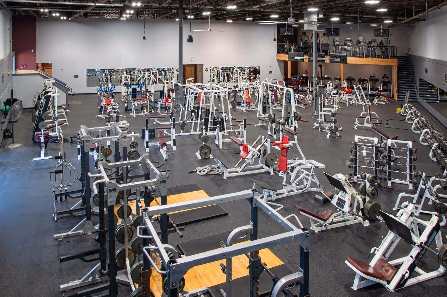 Spacious gym interior with various weightlifting machines and free weights arranged on rubber flooring under bright lighting.