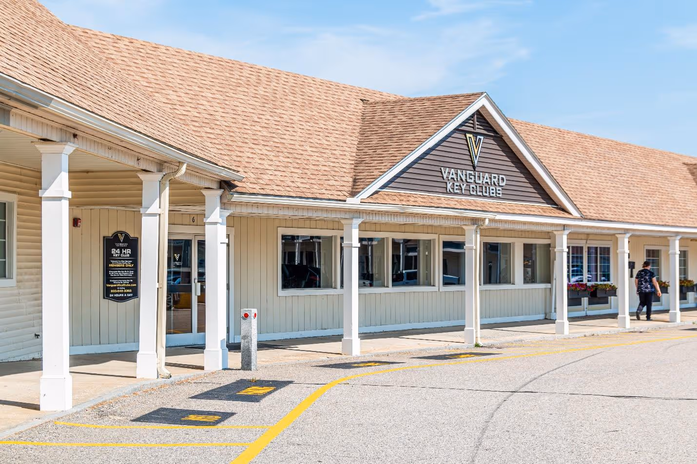 Exterior of Vanguard Key Clubs building with beige siding, brown shingle roof, and white columns under blue sky.