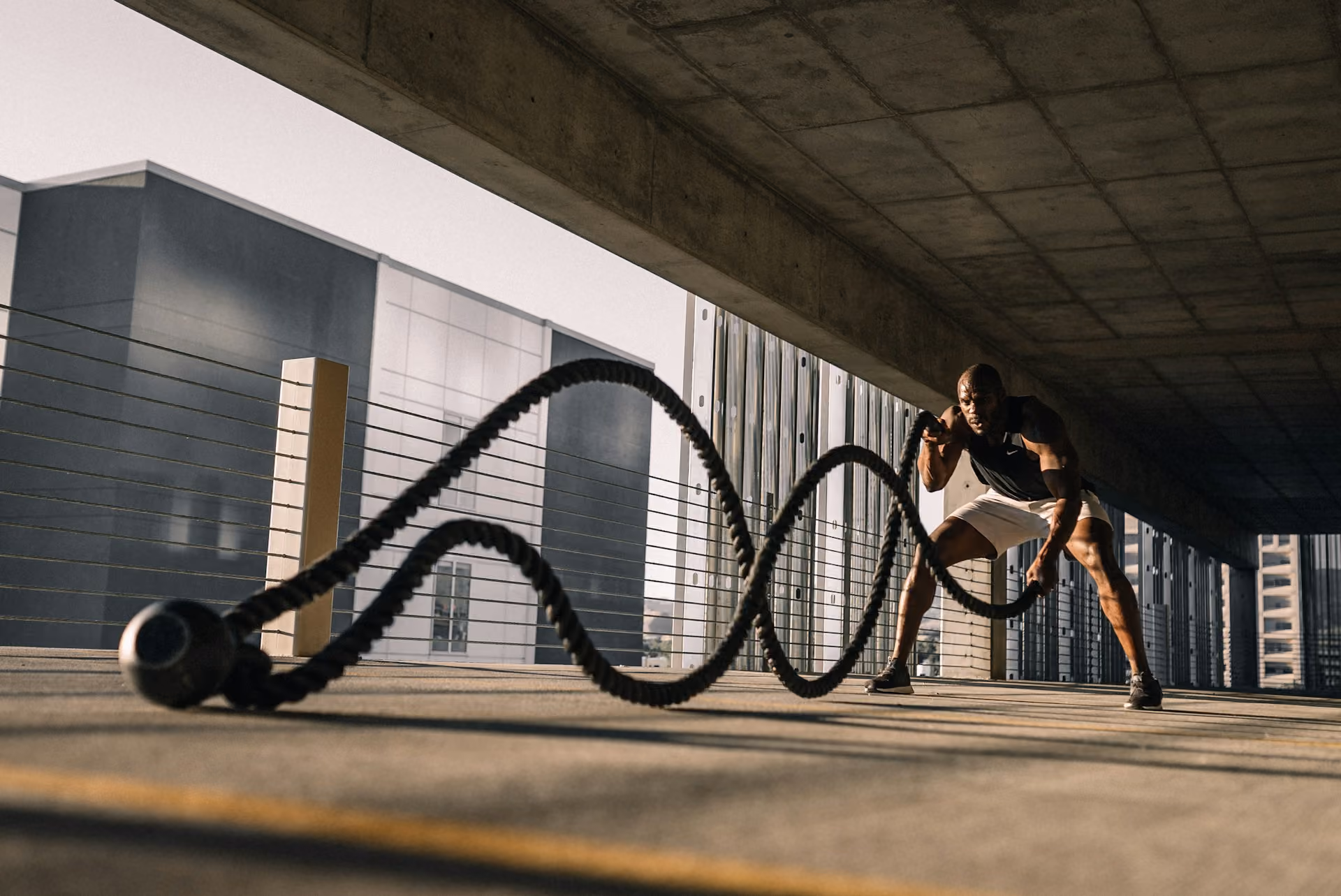 A black man using battle ropes in a parking garage