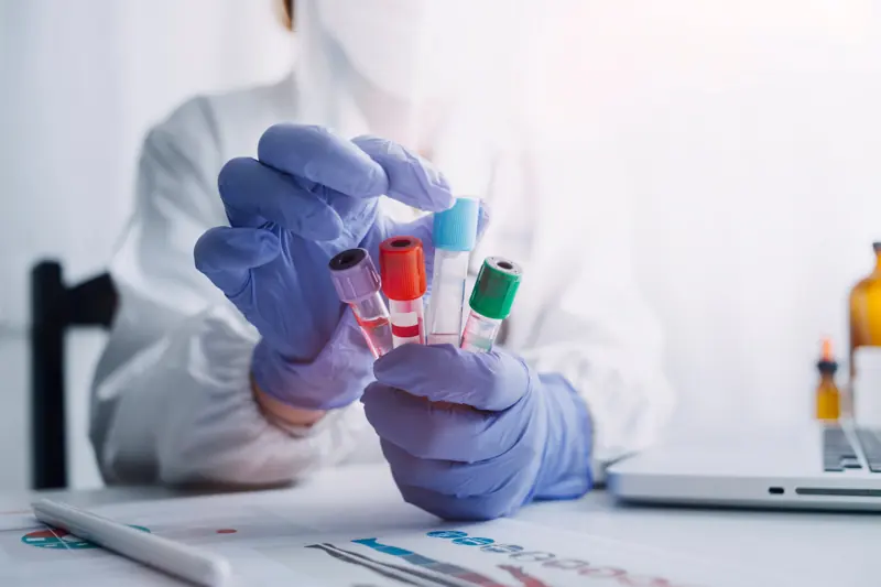 A gloved hand holding blood sample tubes in a laboratory
