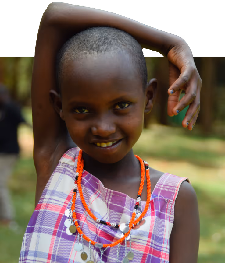 Smiling young child wearing a purple plaid dress and beaded orange necklaces, with one arm raised behind their head.