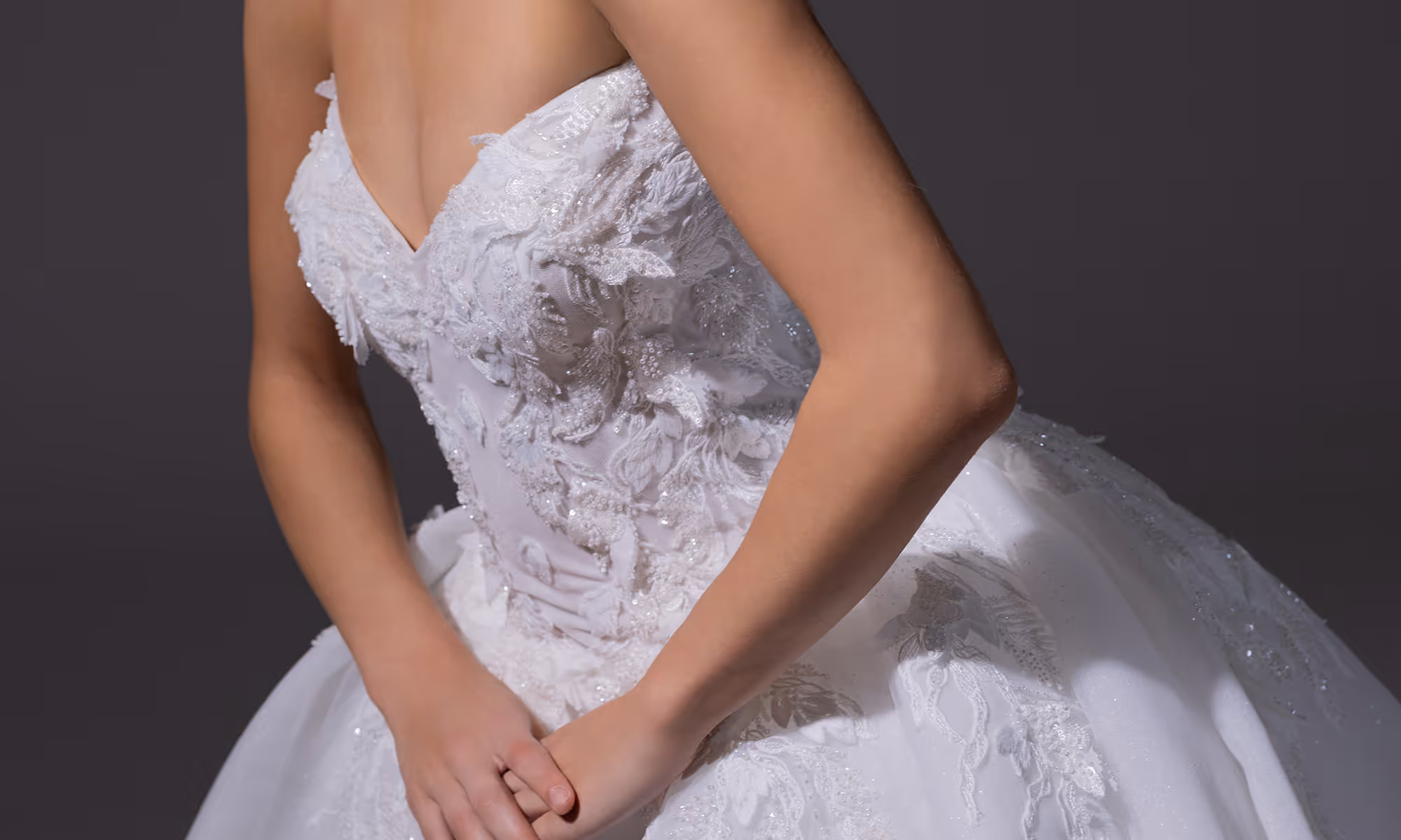 Close-up van een vrouw in een witte kanten en geborduurde trouwjurk met handen gevouwen voor haar.