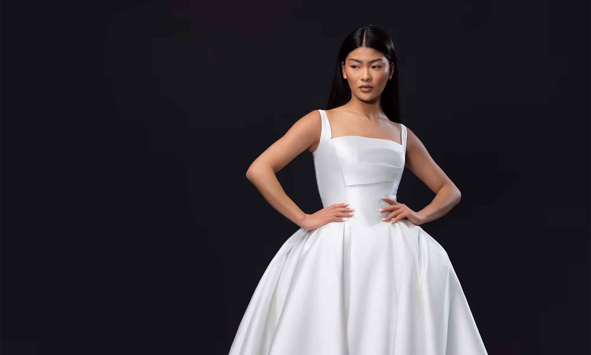 Vrouw in een elegante witte bruidsjurk met een vierkante halslijn, poserend tegen een zwarte achtergrond.