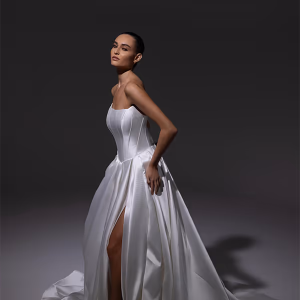 Vrouw poseert in een elegante witte strapless avondjurk met een hoge split tegen een donkere achtergrond.