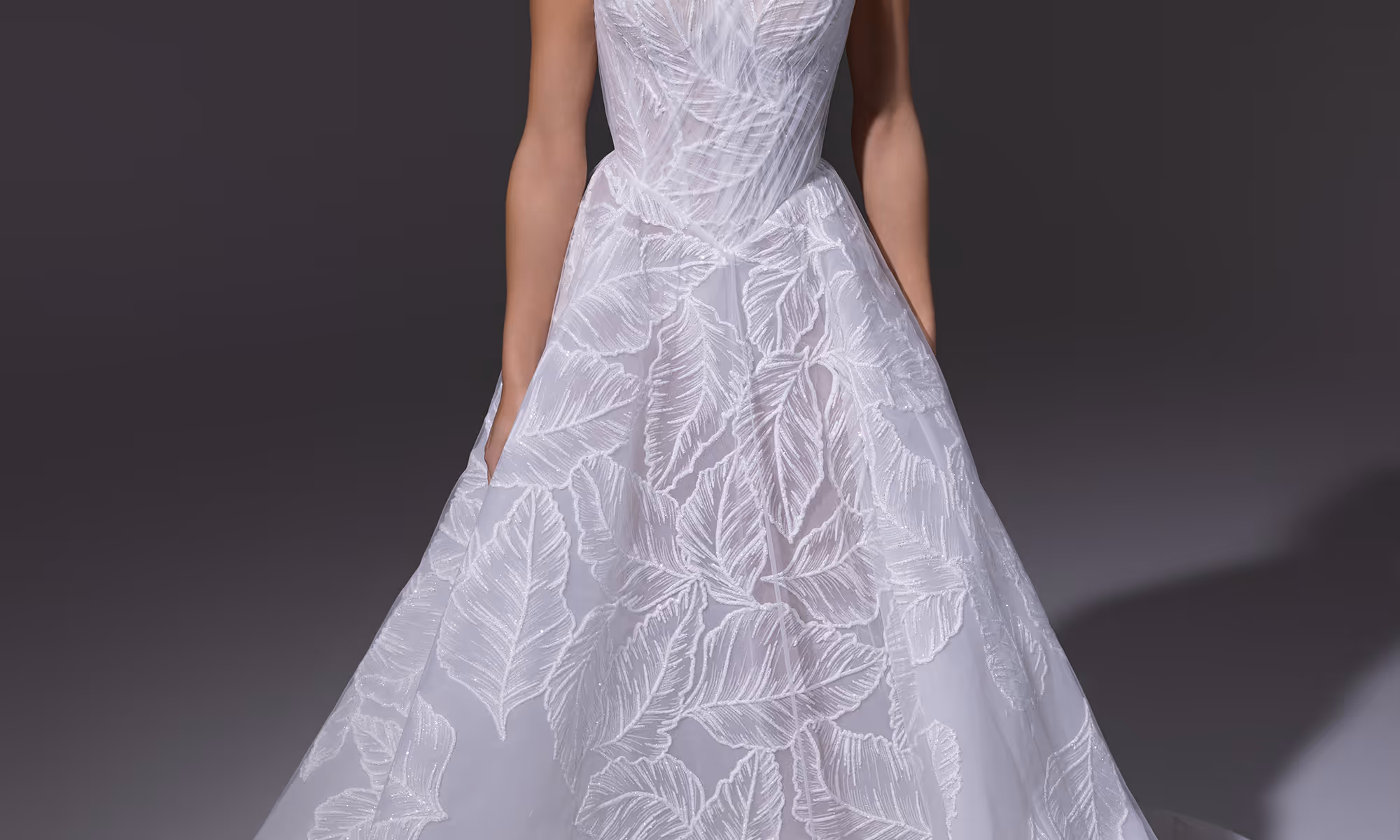 Witte trouwjurk met geplooide details bovenaan en borduursel van grote bladeren op de rok.