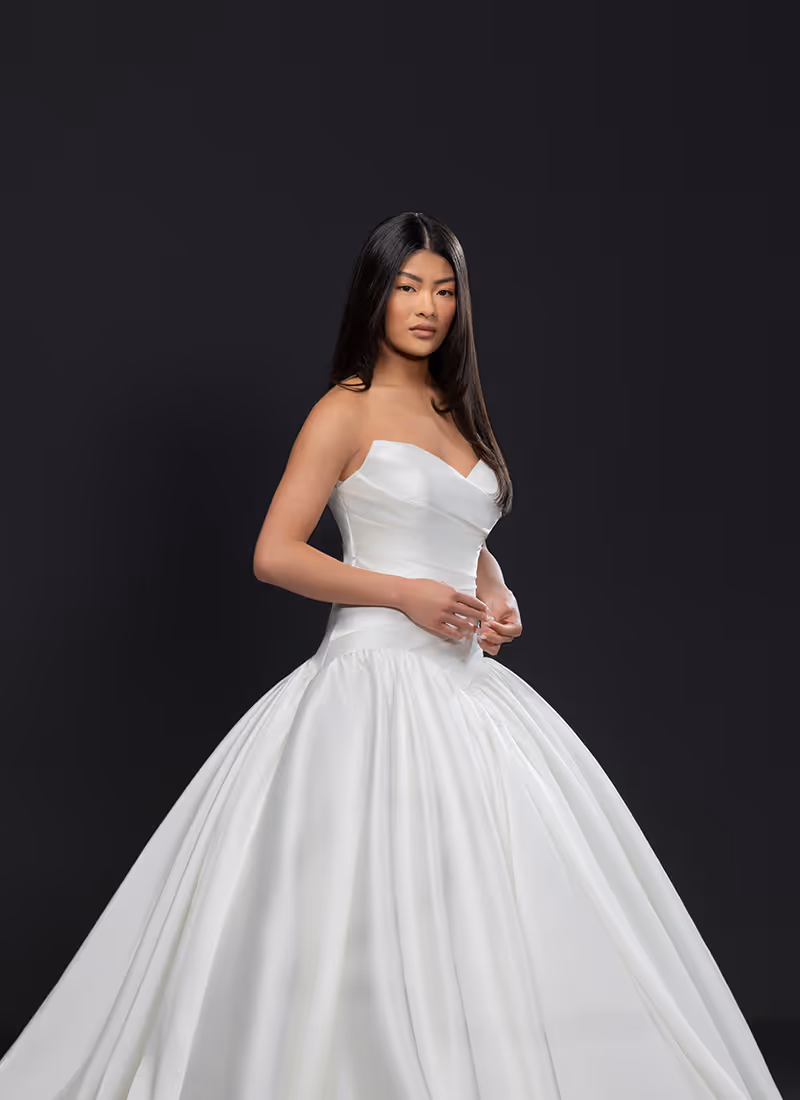 Vrouw met lang zwart haar in strapless witte baljurk met volle rok tegen een zwarte achtergrond.