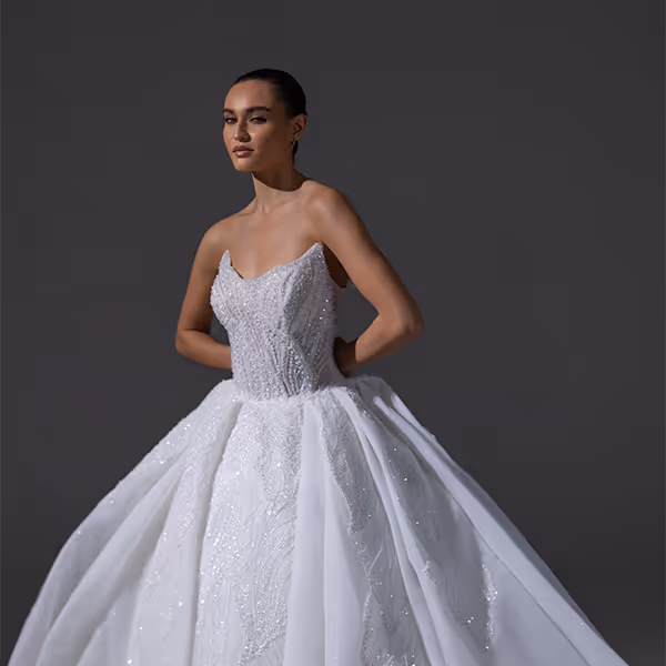 Vrouw in een strapless, wit, glinsterend baljurk met een volumineuze rok tegen een donkere achtergrond.