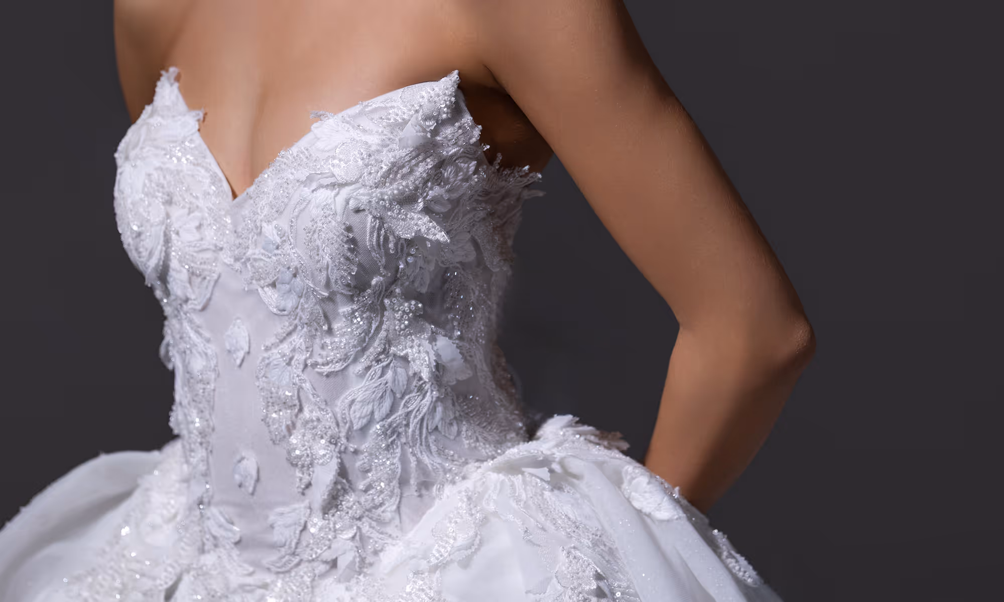 Detail van wit kanten trouwjurk met kralen en borduurwerk op torso en rok.