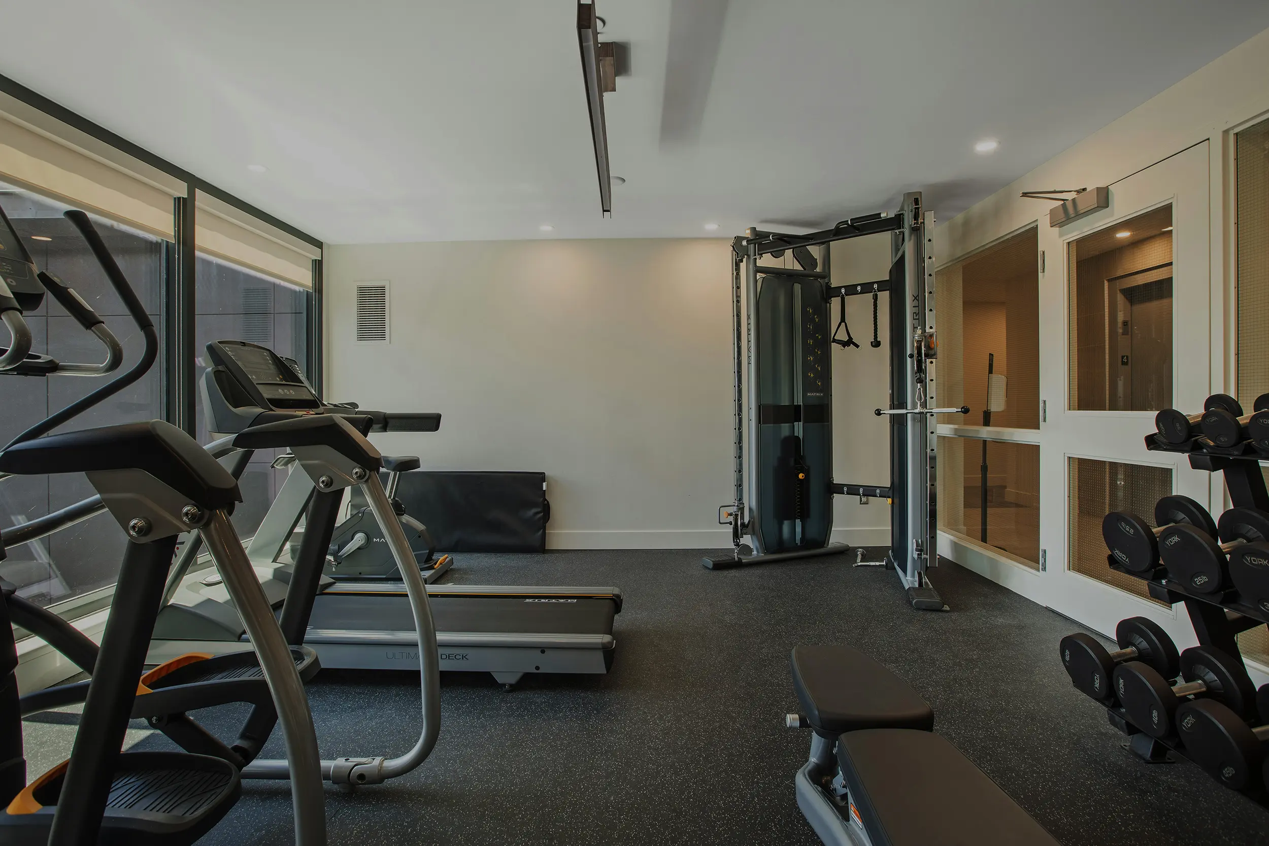 Modern gym with treadmills, elliptical machine, weight bench, dumbbells, and a multi-functional cable machine.