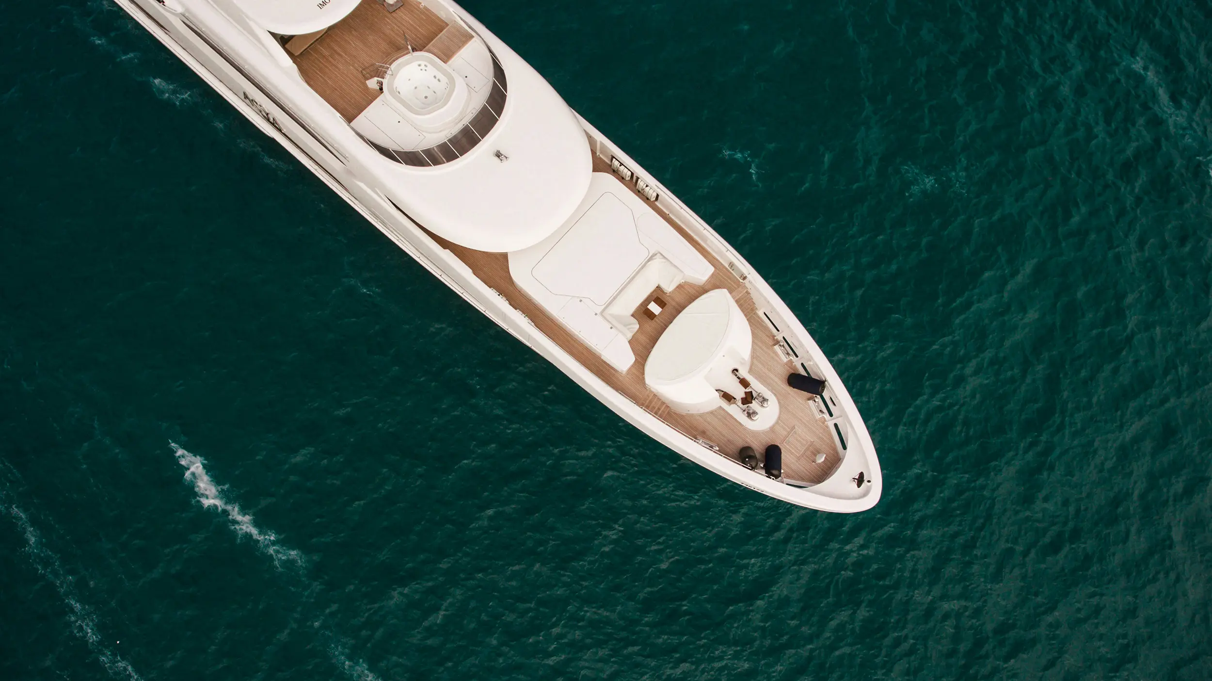 Aerial view of the front deck of a white luxury yacht floating on deep blue water.