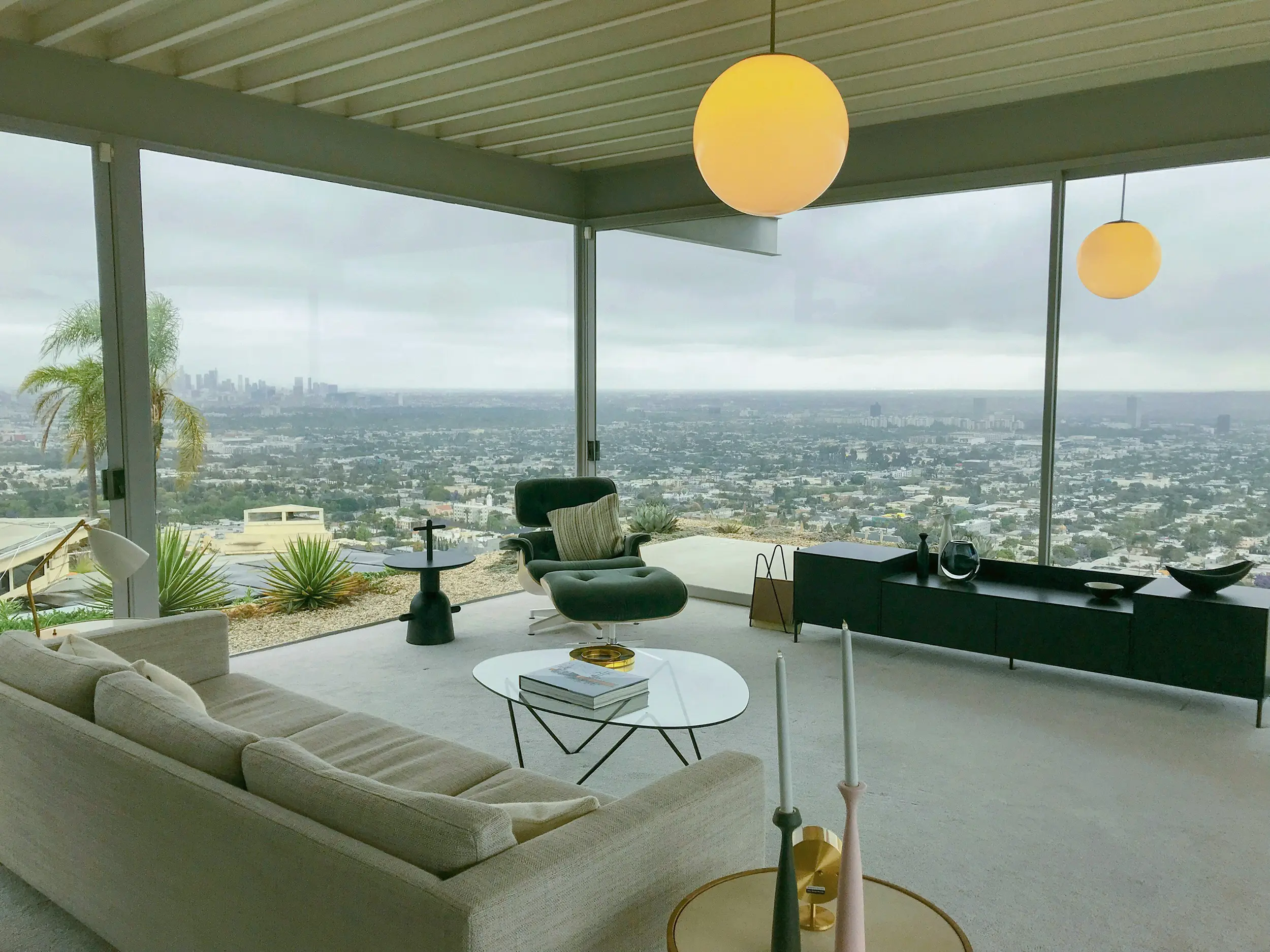 Modern living room with beige sofa, black lounge chair, and large windows overlooking a cityscape.
