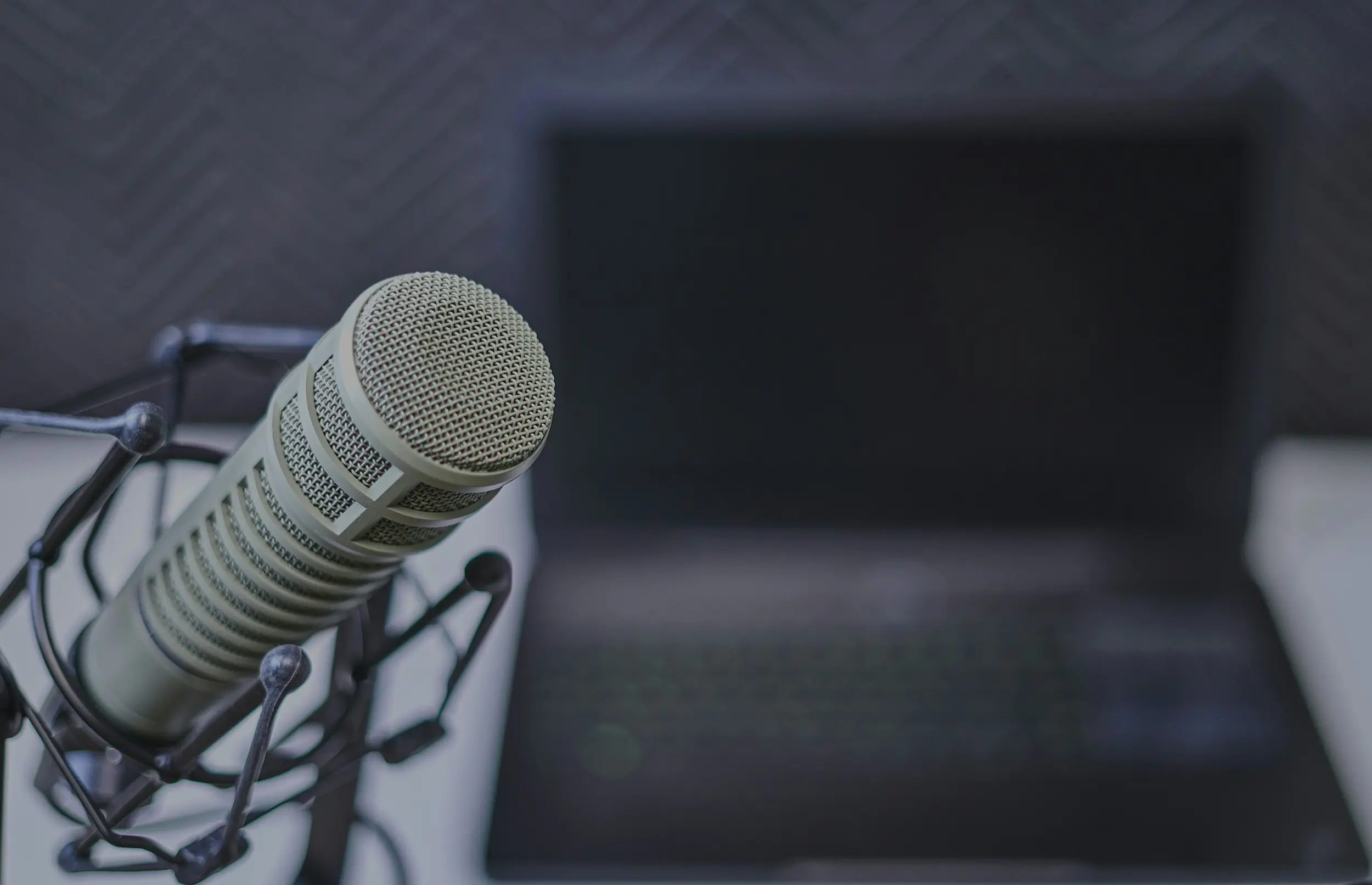 Close-up of a studio microphone with a blurred laptop in the background.