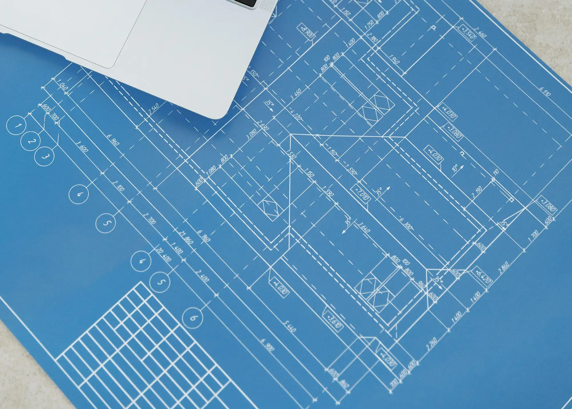 Architectural blueprint with detailed measurements and a partial view of a silver laptop.